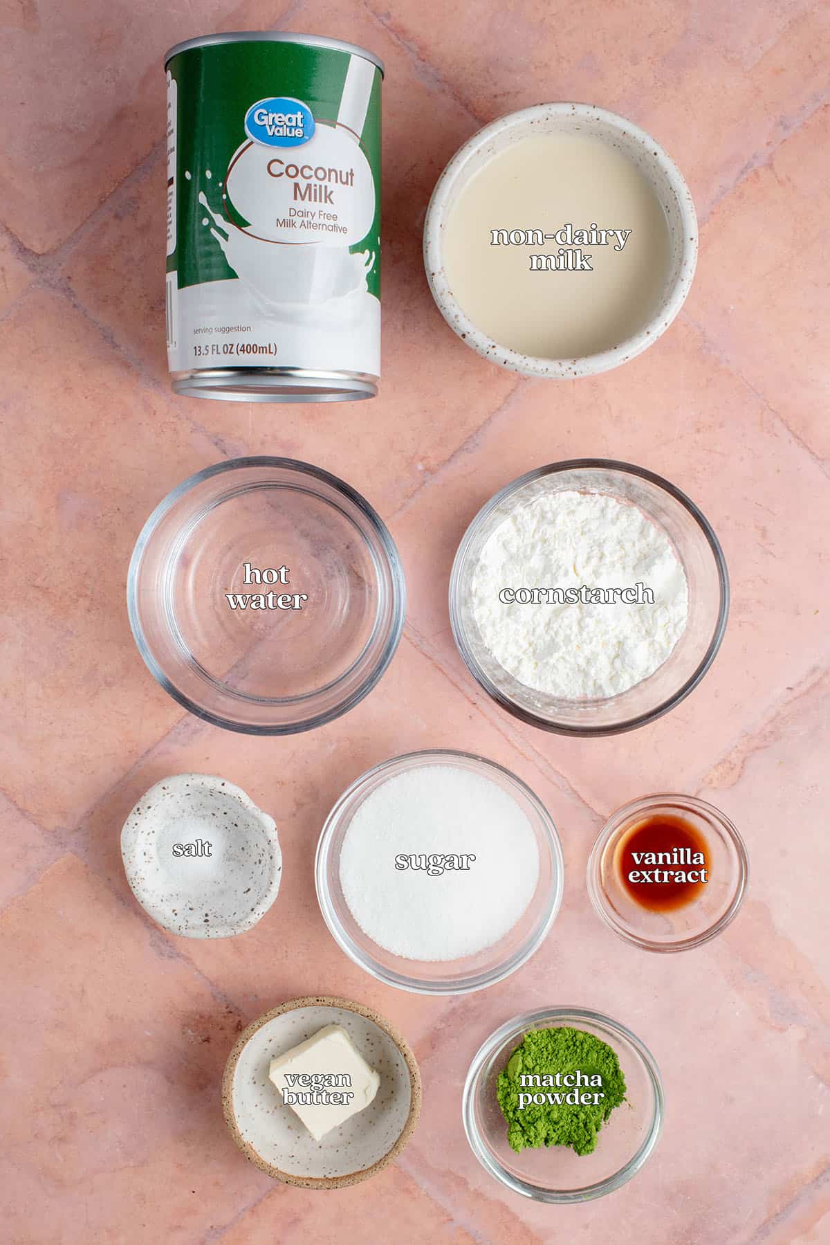 labeled ingredients of Vegan Matcha Crème Brûlée on pink table: coconut milk, non-dairy milk, hot water, cornstarch, salt, sugar, vanilla extract, vegan butter and matcha powder