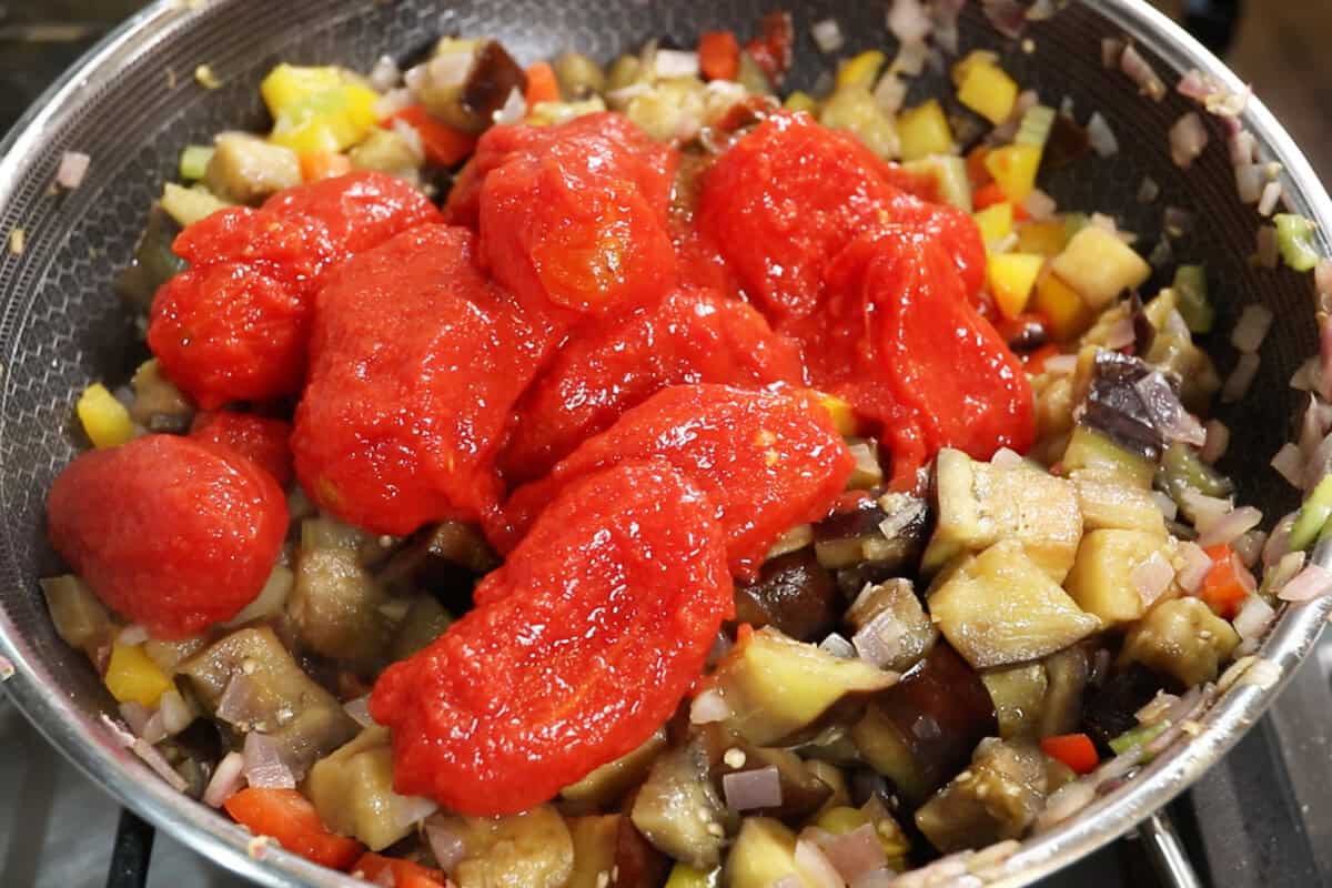 adding tomatoes to Eggplant Caponata in a large wok