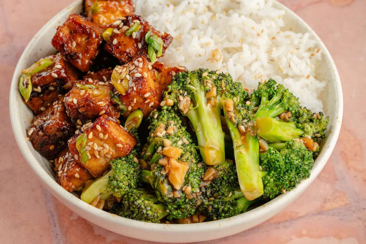 horizontal photo of 10-Minute Broccoli with Garlic Sauce in white bowl with rice and tofu