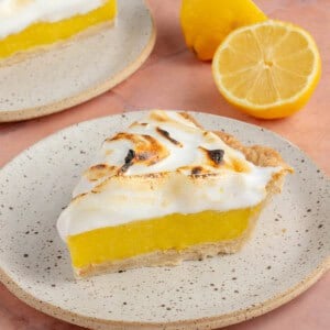 lemon meringue pie slices on small white plates with fresh lemons on pink table