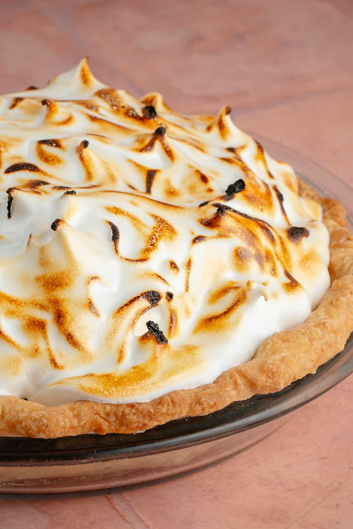 egg-free vegan lemon meringue pie in glass pan on pink table in glass pie pan