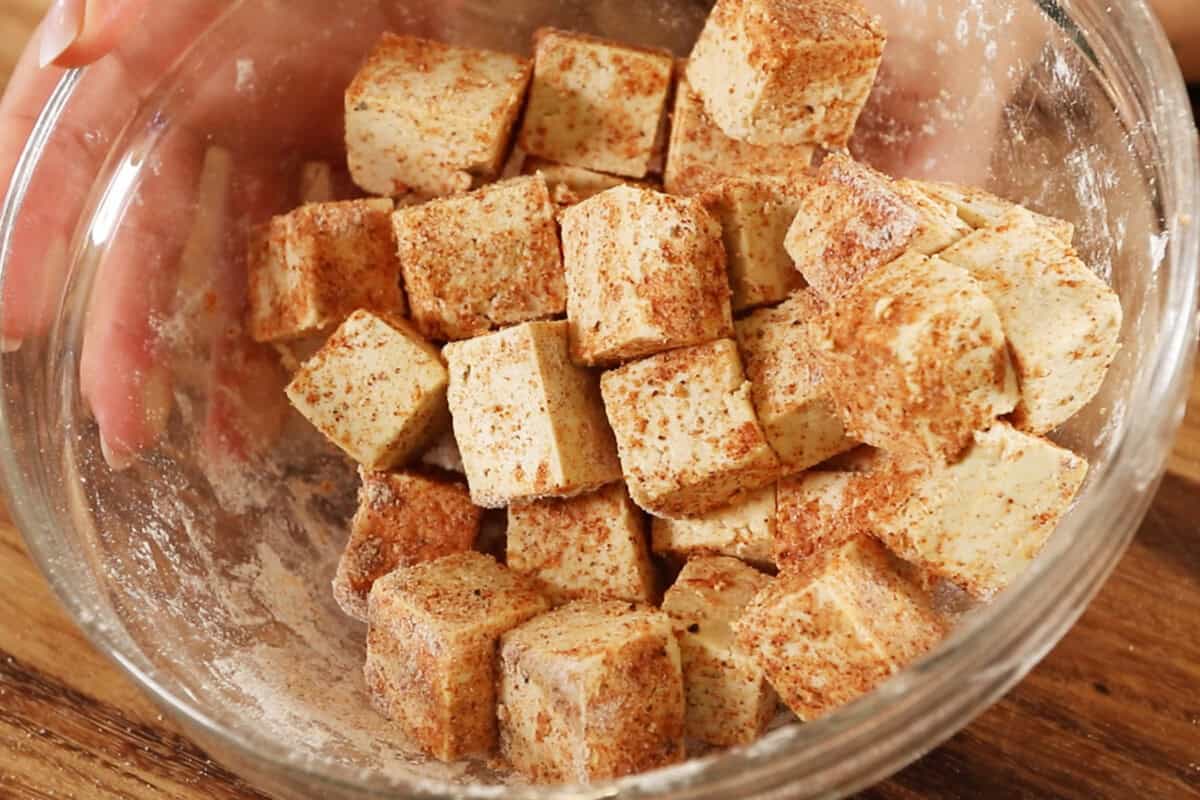 mixing a bowl of cubed tofu with cornstarch and spices