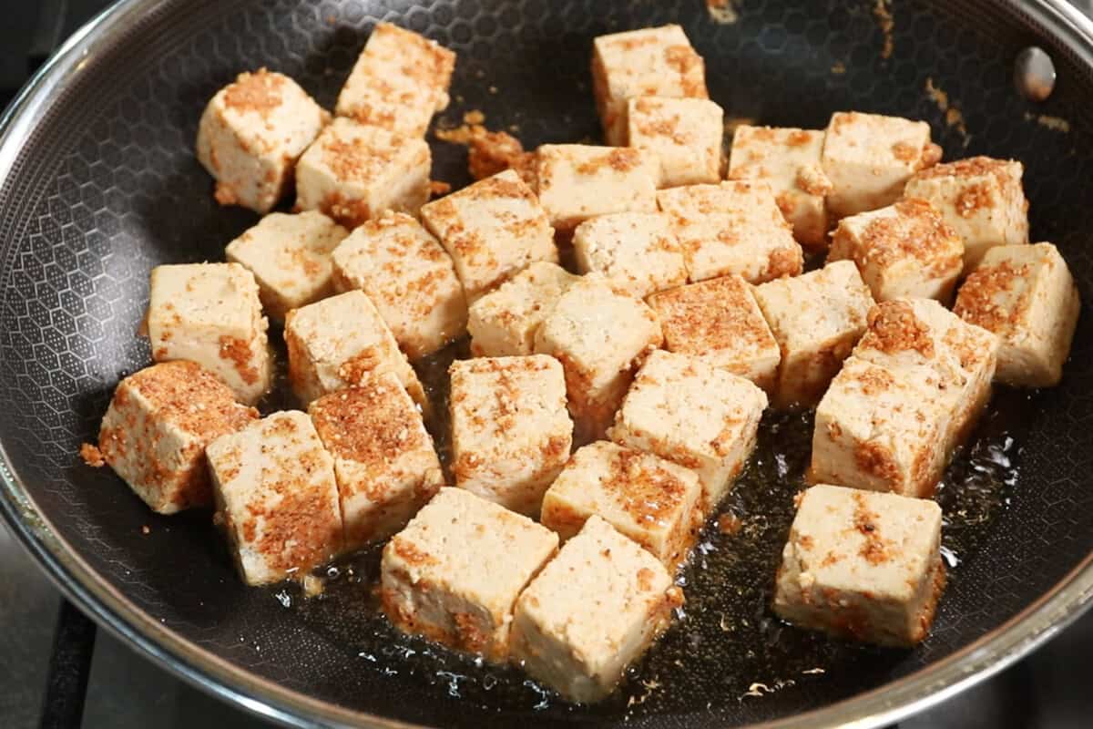 cornstarch and spiced tofu frying in a skillet with oil
