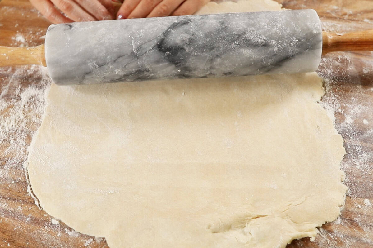rolling out pie dough on wooden board with marble rolling pin