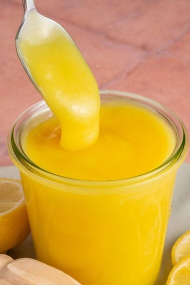 A spoonful of lemon curd being poured into a bowl.