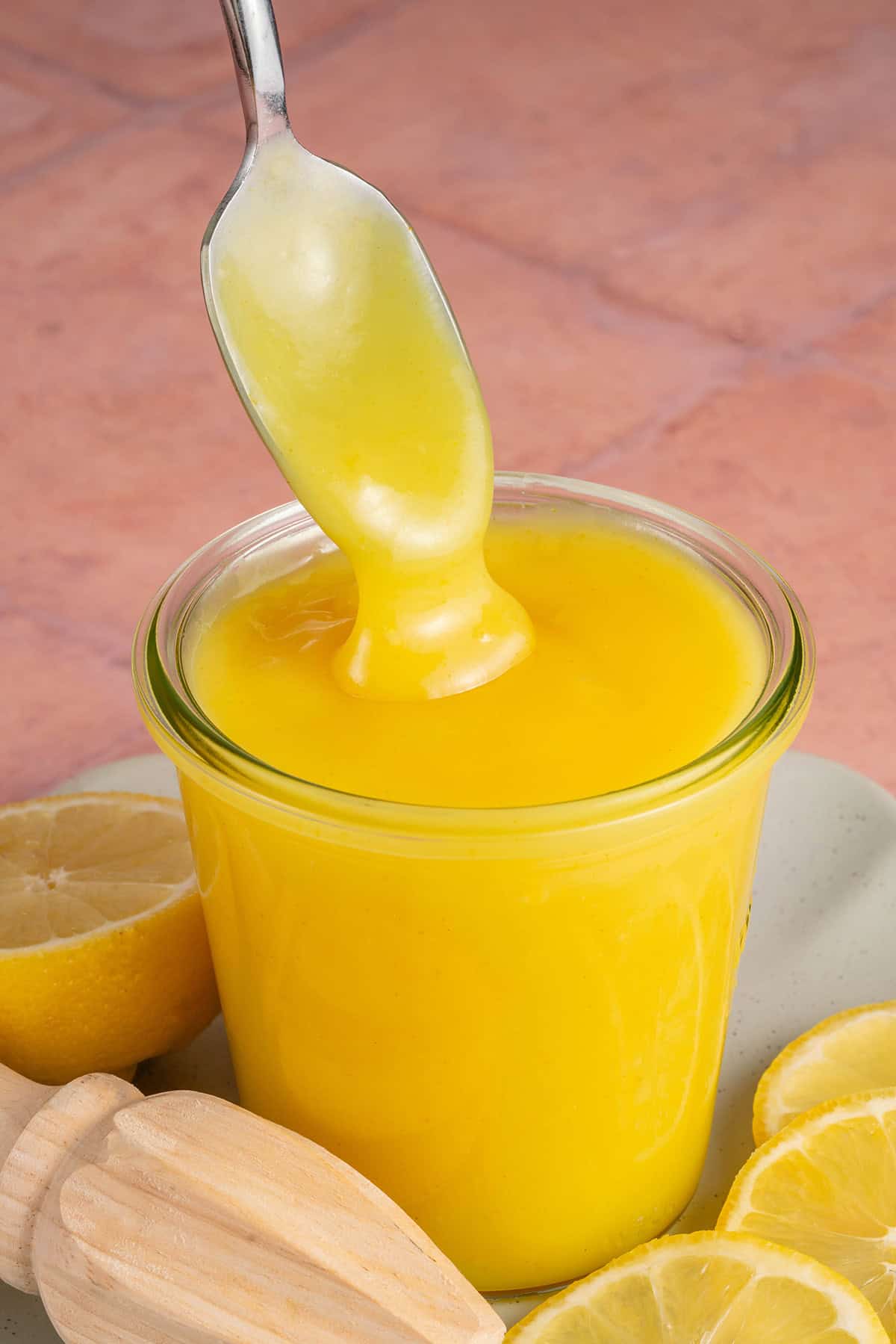 a metal spoon scooping vegan lemon curd out of a glass jar 