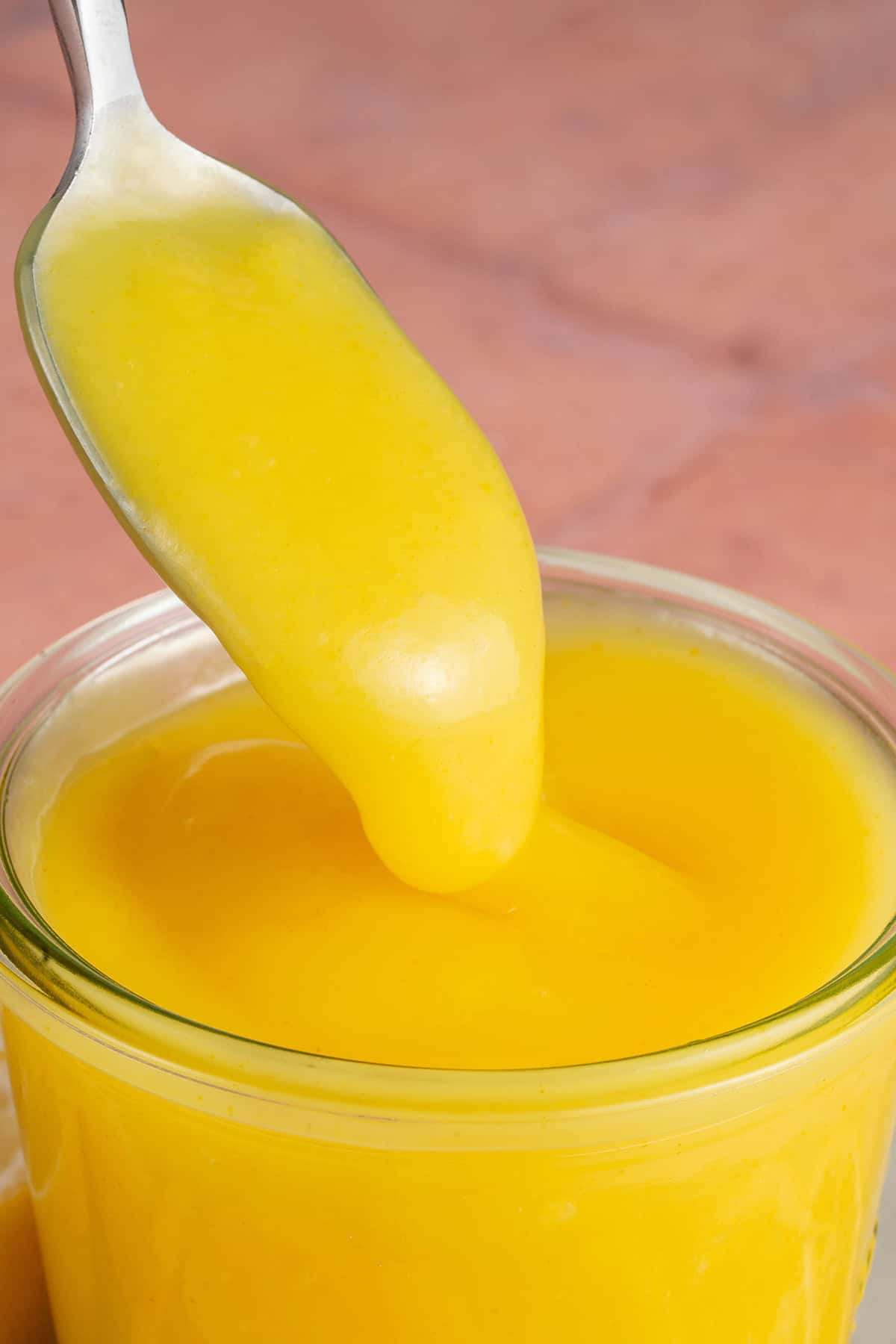 A spoonful of lemon curd being poured into a jar.