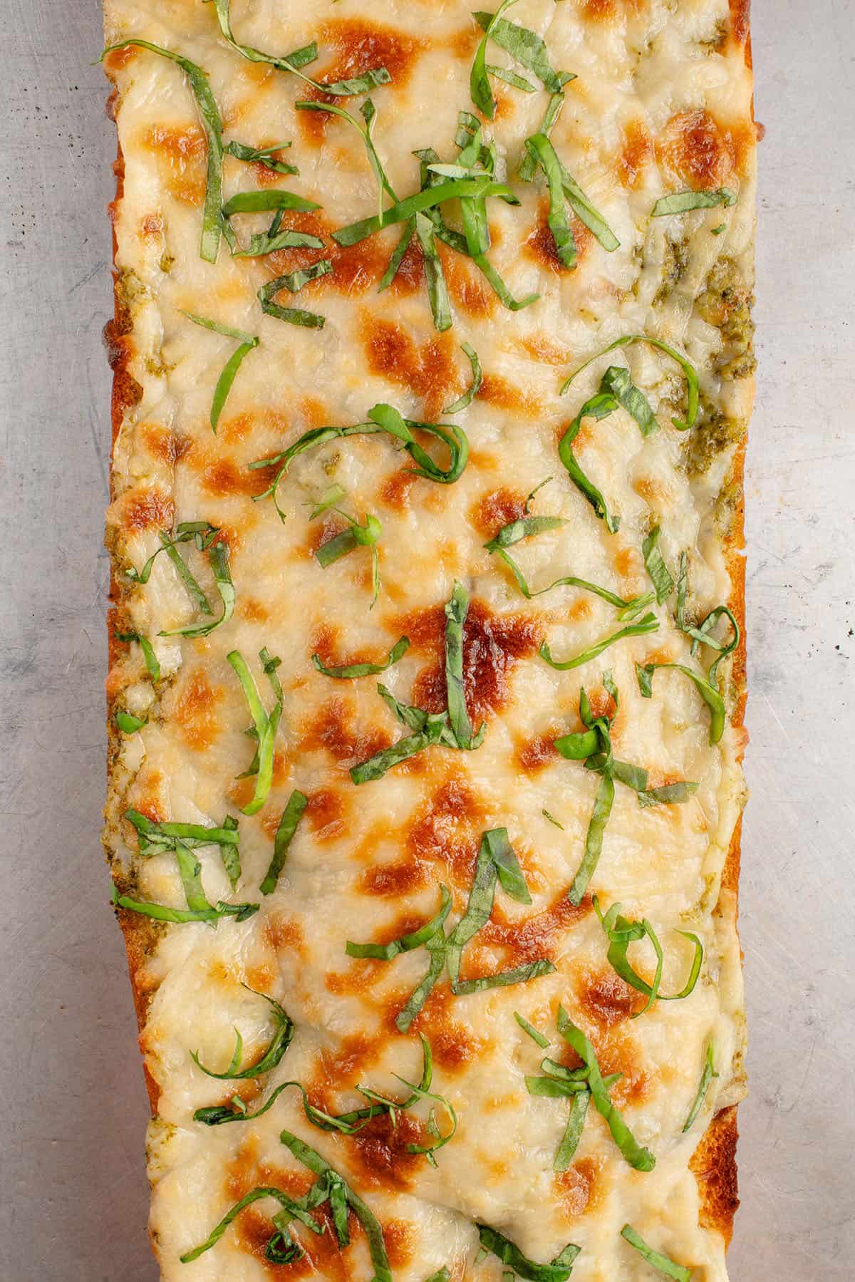 cheesy pesto garlic bread topped with fresh basil