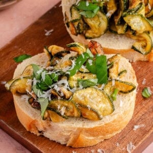 fried zucchini on sliced bread topped with vegan parmesan and sliced basil