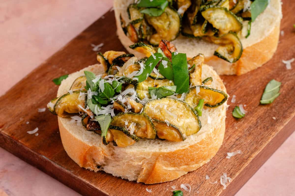 fried zucchini on sliced bread topped with vegan parmesan and sliced basil