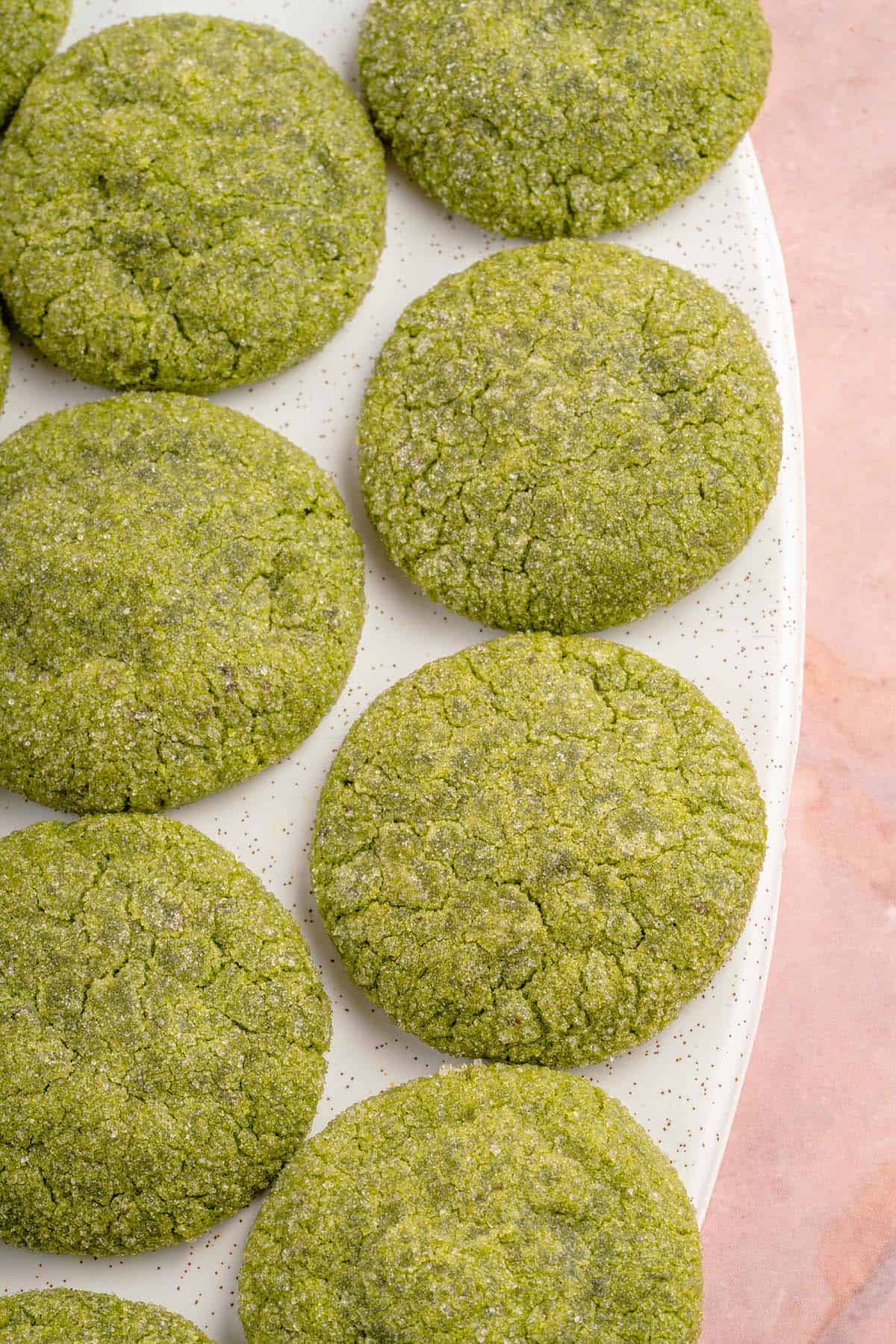 close up photo of vegan matcha sugar cookies on a white platter and pink backdrop