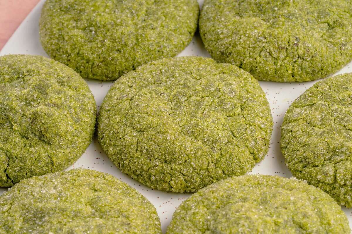 horizontal photo of vegan matcha sugar cookies on a white platter and pink backdrop