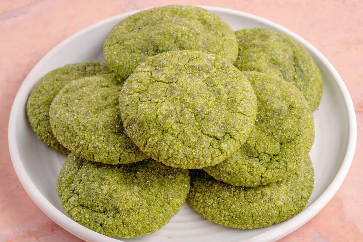 white plate with a stack of vegan matcha sugar cookies on a pink table