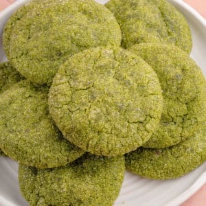 close up photo of a stack of vegan matcha sugar cookies on a white plate and pink backdrop