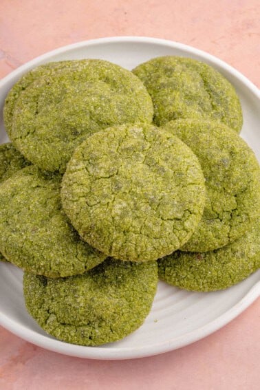 close up photo of a stack of vegan matcha sugar cookies on a white plate and pink backdrop