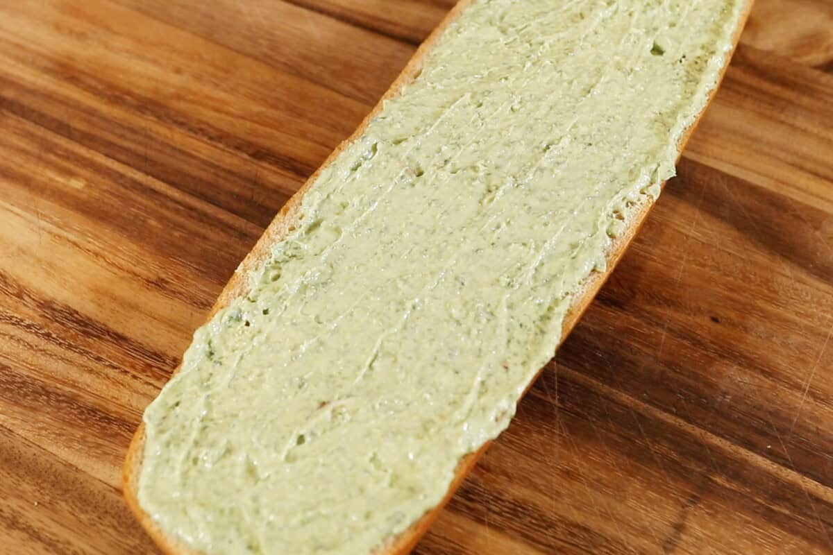 spreading pesto garlic butter on a half of french bread