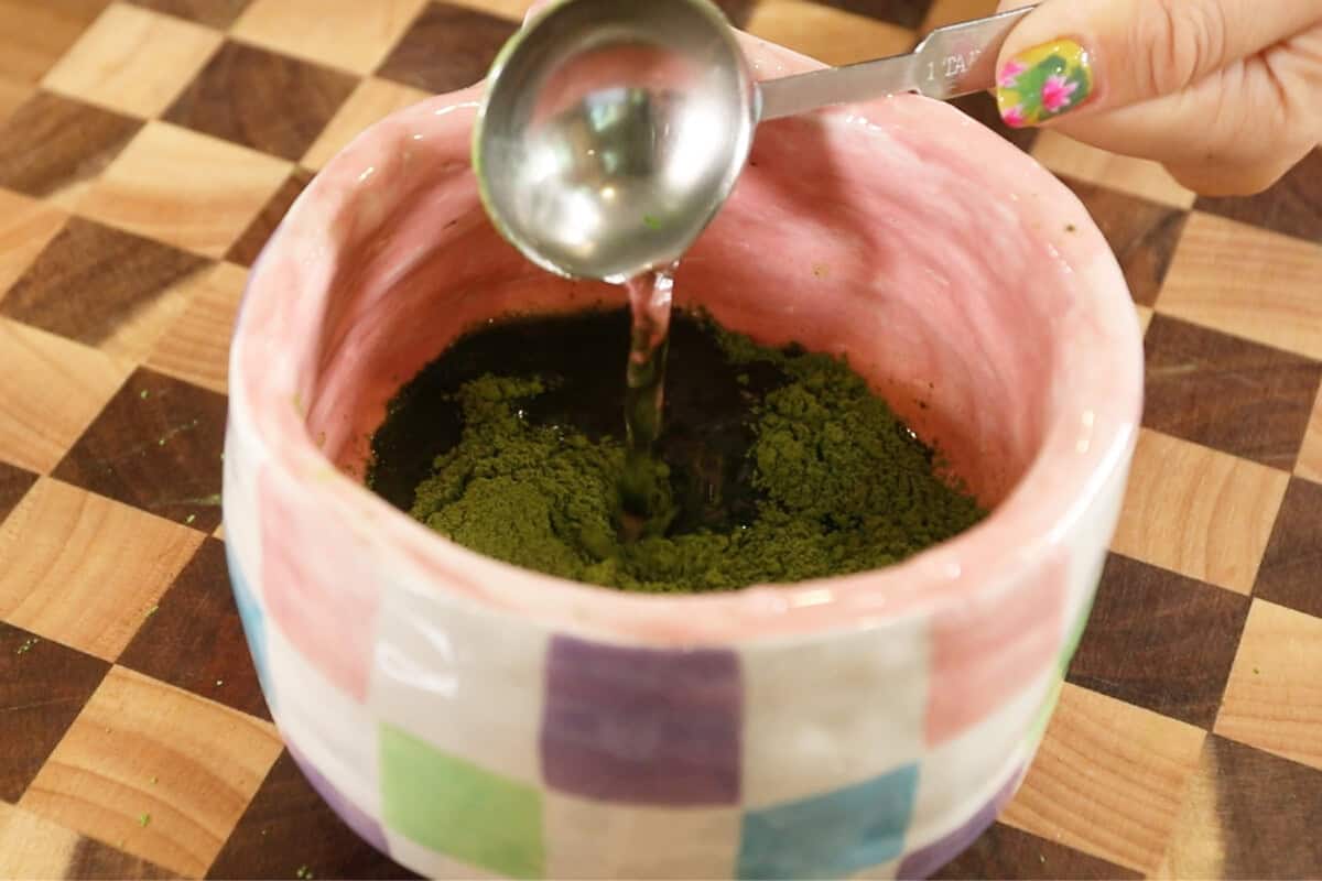 adding hot water to a pink bowl with matcha powder