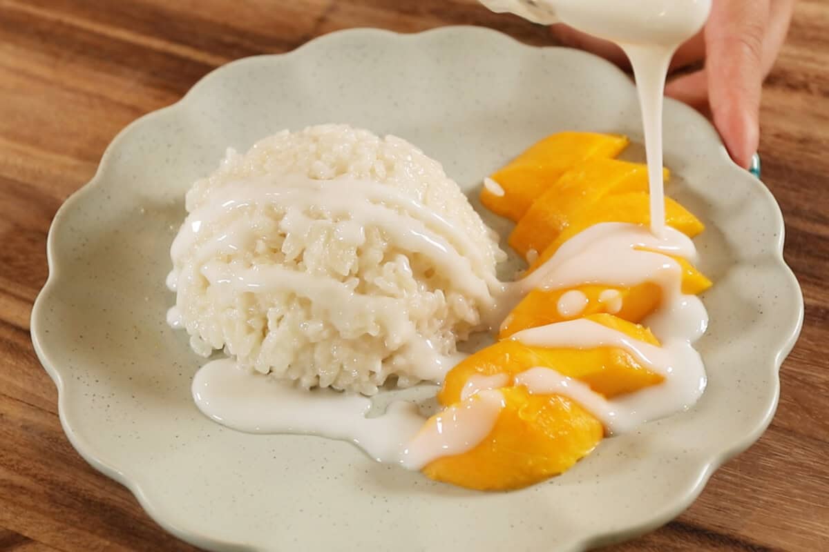 pouring sweet coconut sauce over mango sticky rice