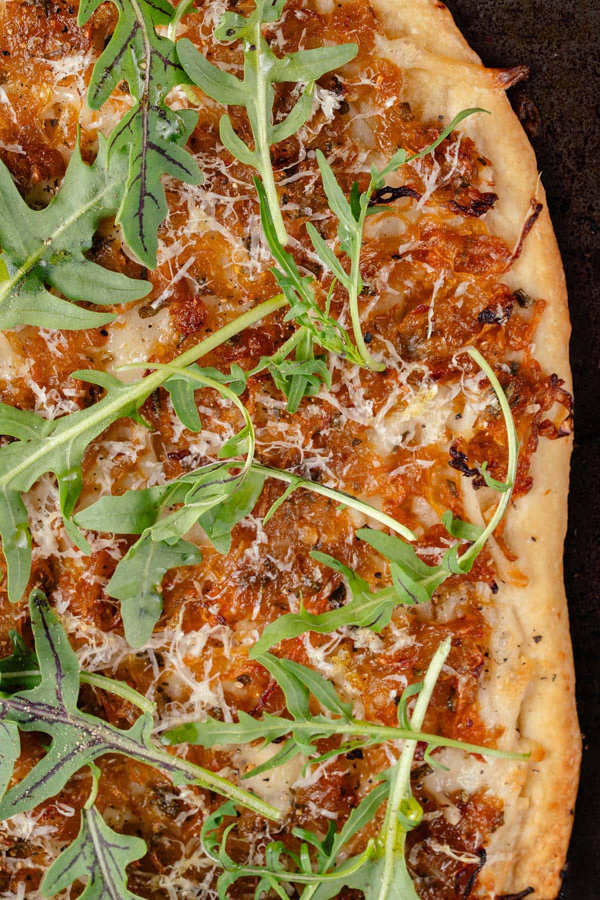 close up photo of vegan caramelized onion flatbread on dark baking sheet with arugula