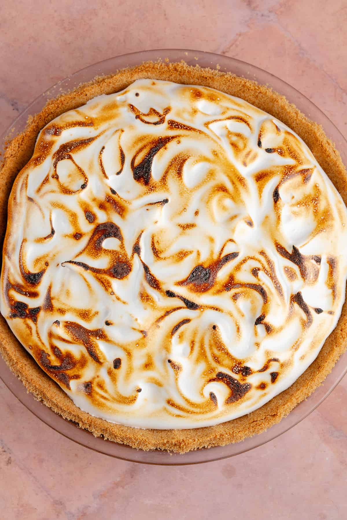 overhead photo of a vegan s'mores pie with a torched meringue topping on a pink surface
