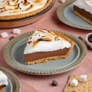 photo of slices of S'mores Pie with toasted meringue topping on blue plates with half of a pie in the background