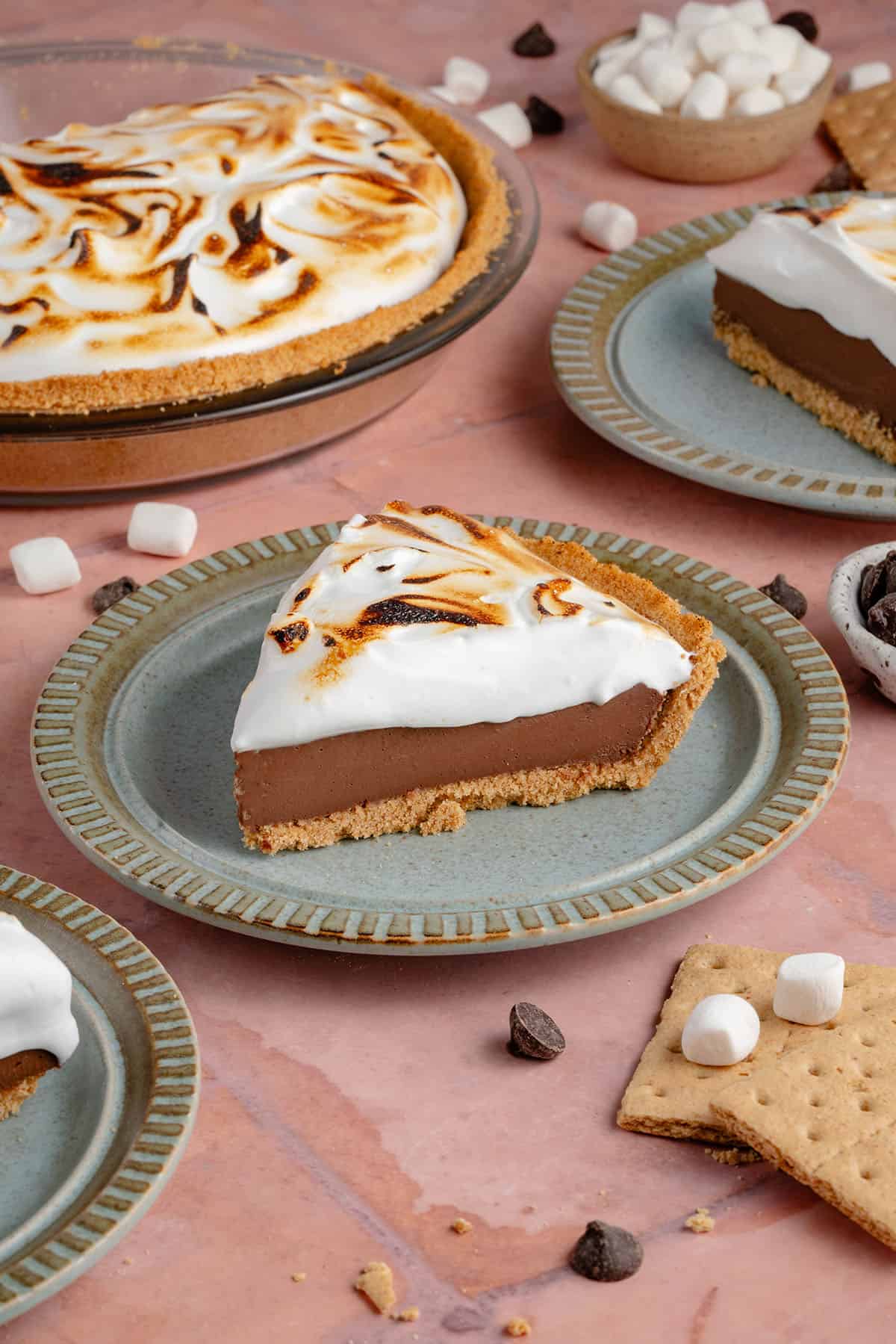 photo of slices of S'mores Pie with toasted meringue topping on blue plates with half of a pie in the background