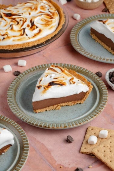 photo of slices of S'mores Pie with toasted meringue topping on blue plates with half of a pie in the background