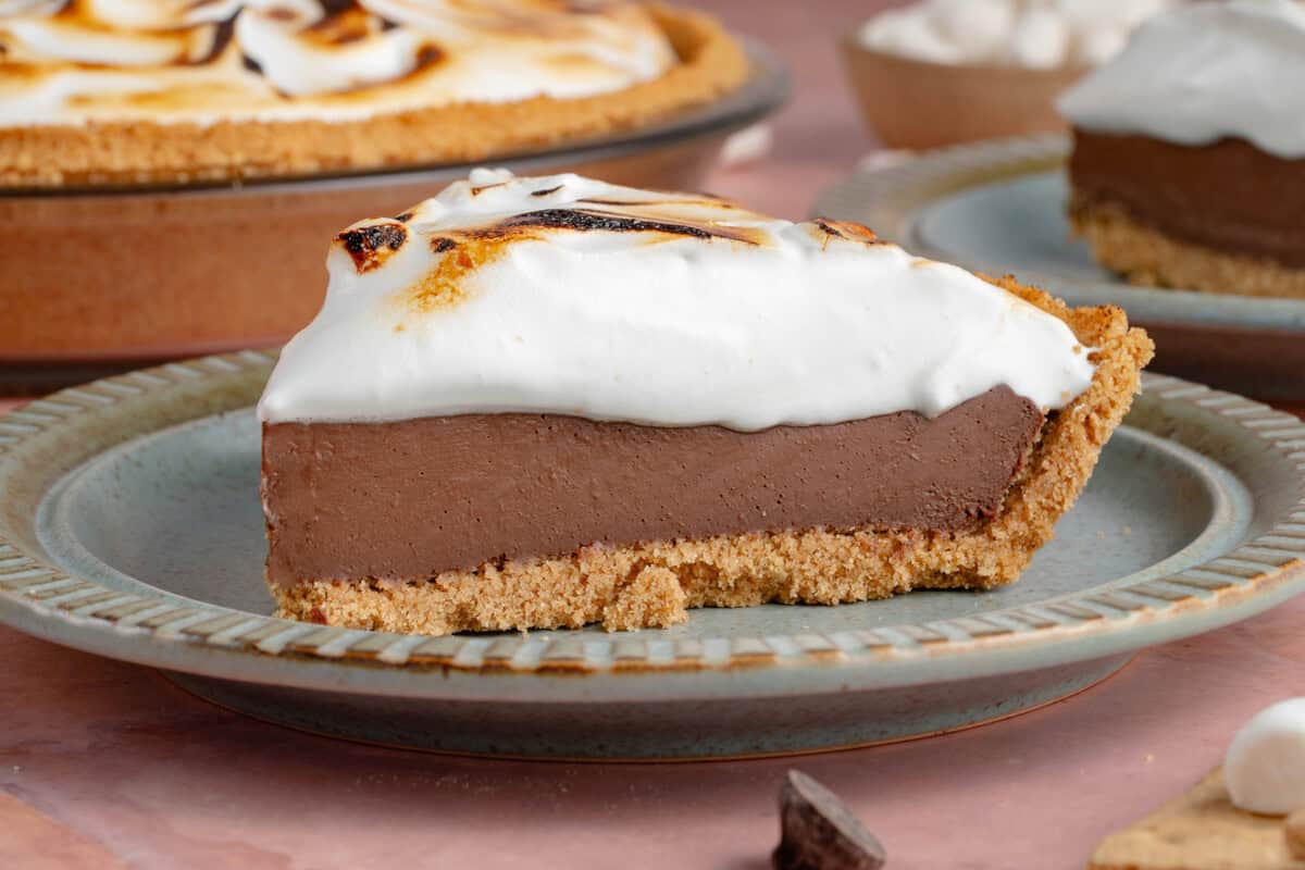 side photo of slice of S'mores Pie with toasted meringue topping on a blue plate with half of a pie in the background