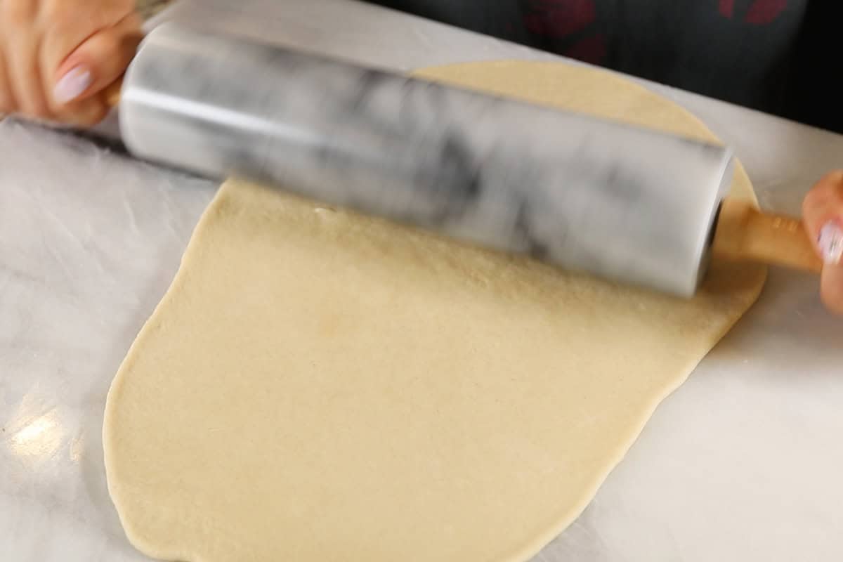 rolling out flatbread dough with rolling pin on marble surface