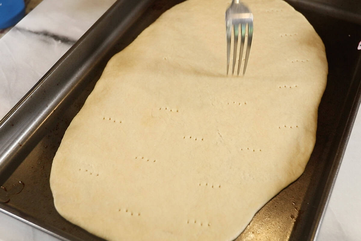 poking holes in plain Flatbread on dark baking sheet before baking