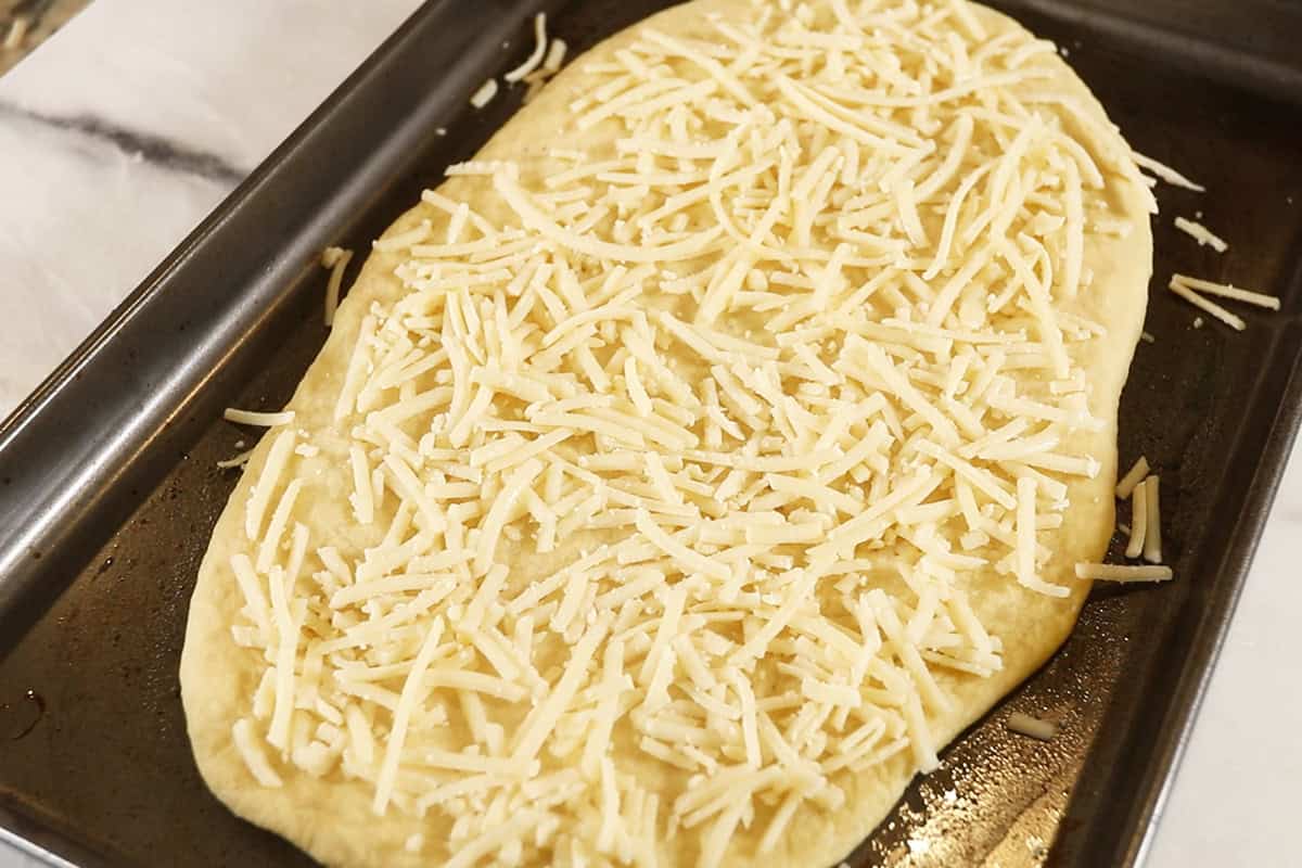 parbaked plain Flatbread with vegan mozzarella cheese on dark baking sheet