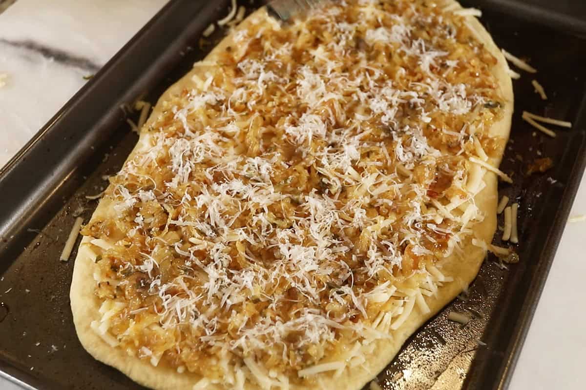 vegan caramelized onion flatbread on dark baking sheet before baking