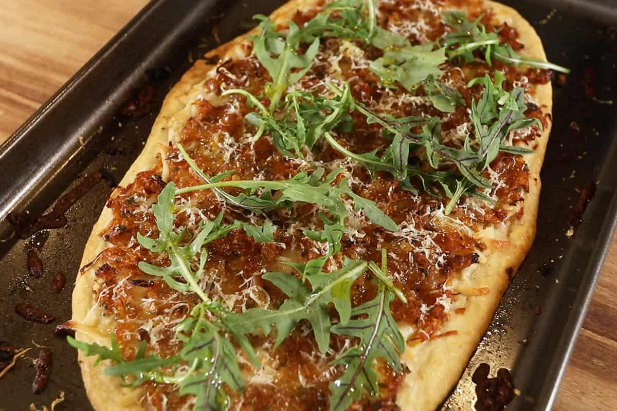 vegan caramelized onion flatbread on dark baking sheet with arugula