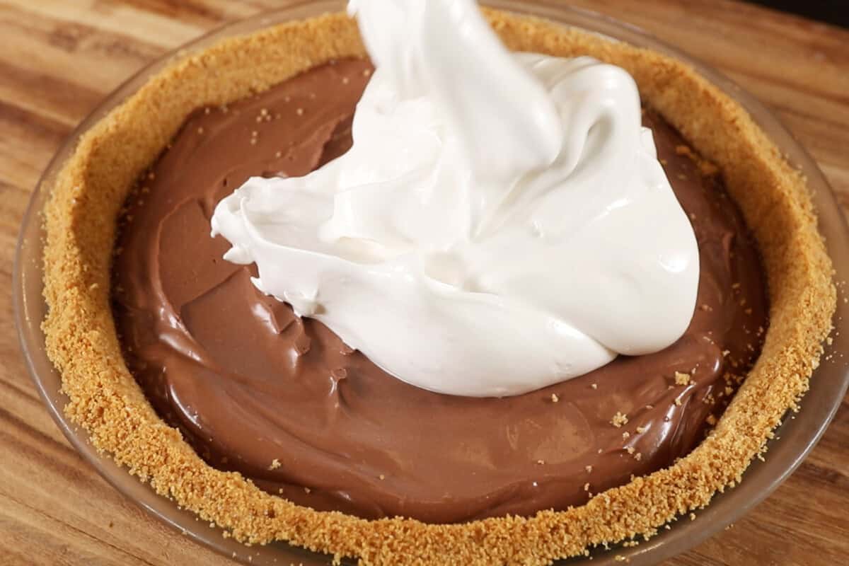 dolloping vegan meringue on top of a vegan s'mores pie