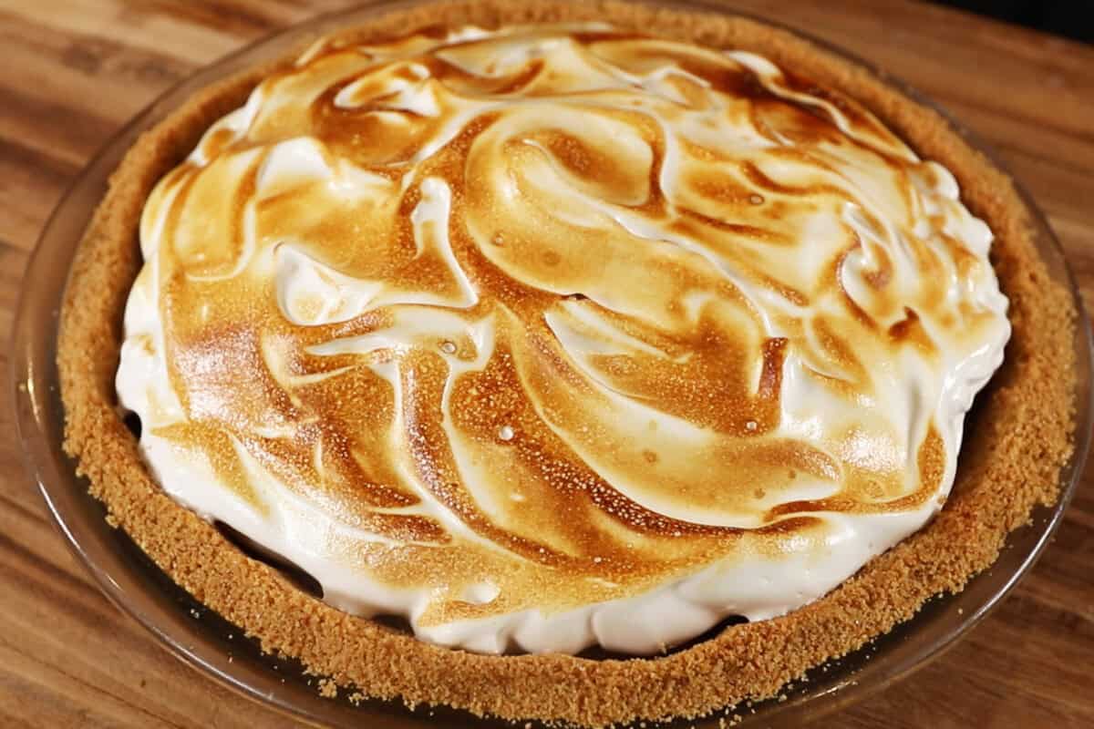photo of a vegan s'mores pie with a torched meringue topping on a wooden surface