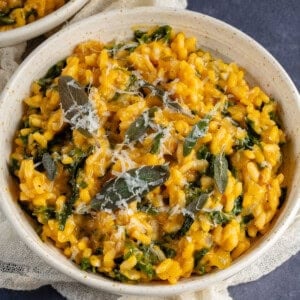 Bowl of butternut squash risotto with kale topped with fried sage and vegan parmesan
