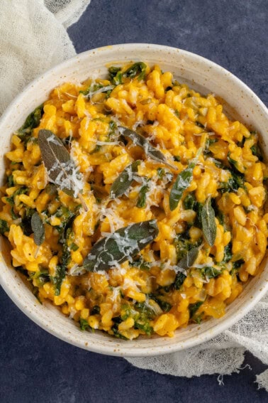 Bowl of butternut squash risotto with kale topped with fried sage and vegan parmesan