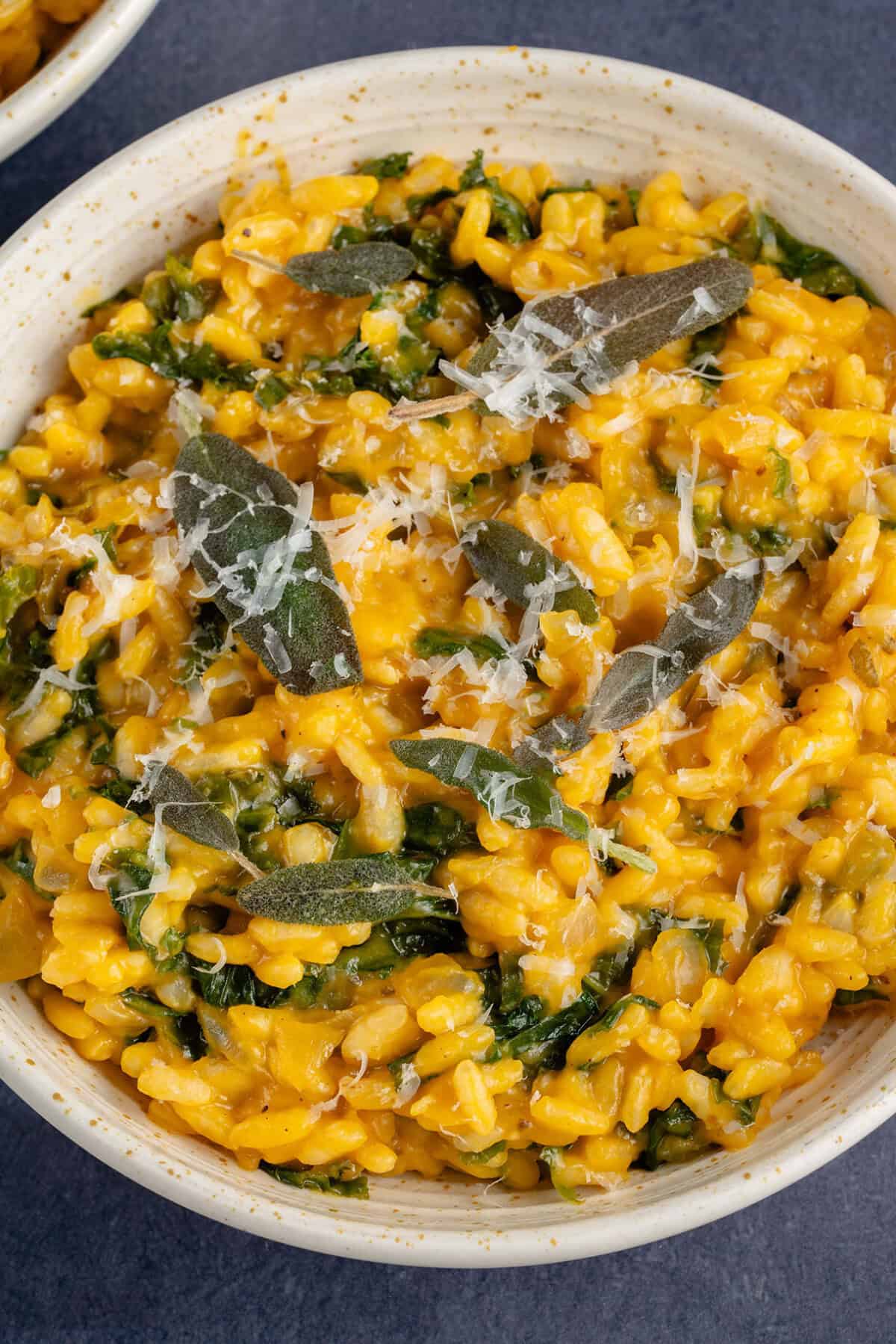 Bowl of butternut squash risotto with kale topped with fried sage and vegan parmesan