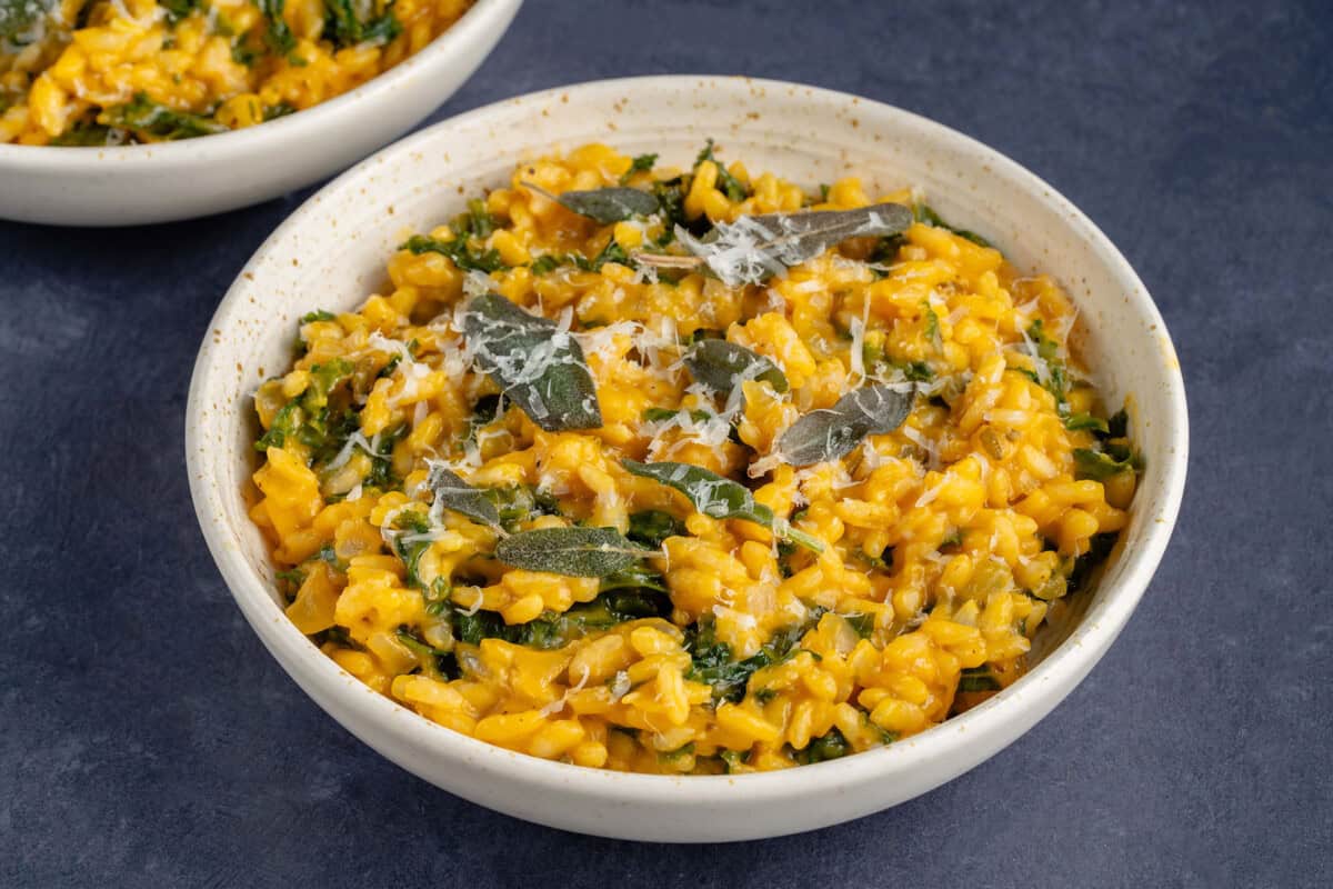 Bowl of butternut squash risotto with kale topped with fried sage and vegan parmesan