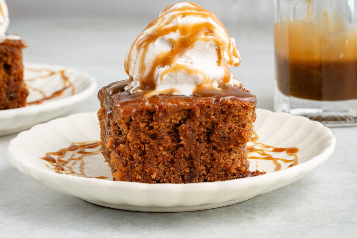 slice of chai sticky toffee pudding topped with ice cream and drizzled with caramel on a white plate