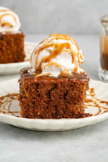 slice of chai sticky toffee pudding topped with ice cream and drizzled with caramel on a white plate