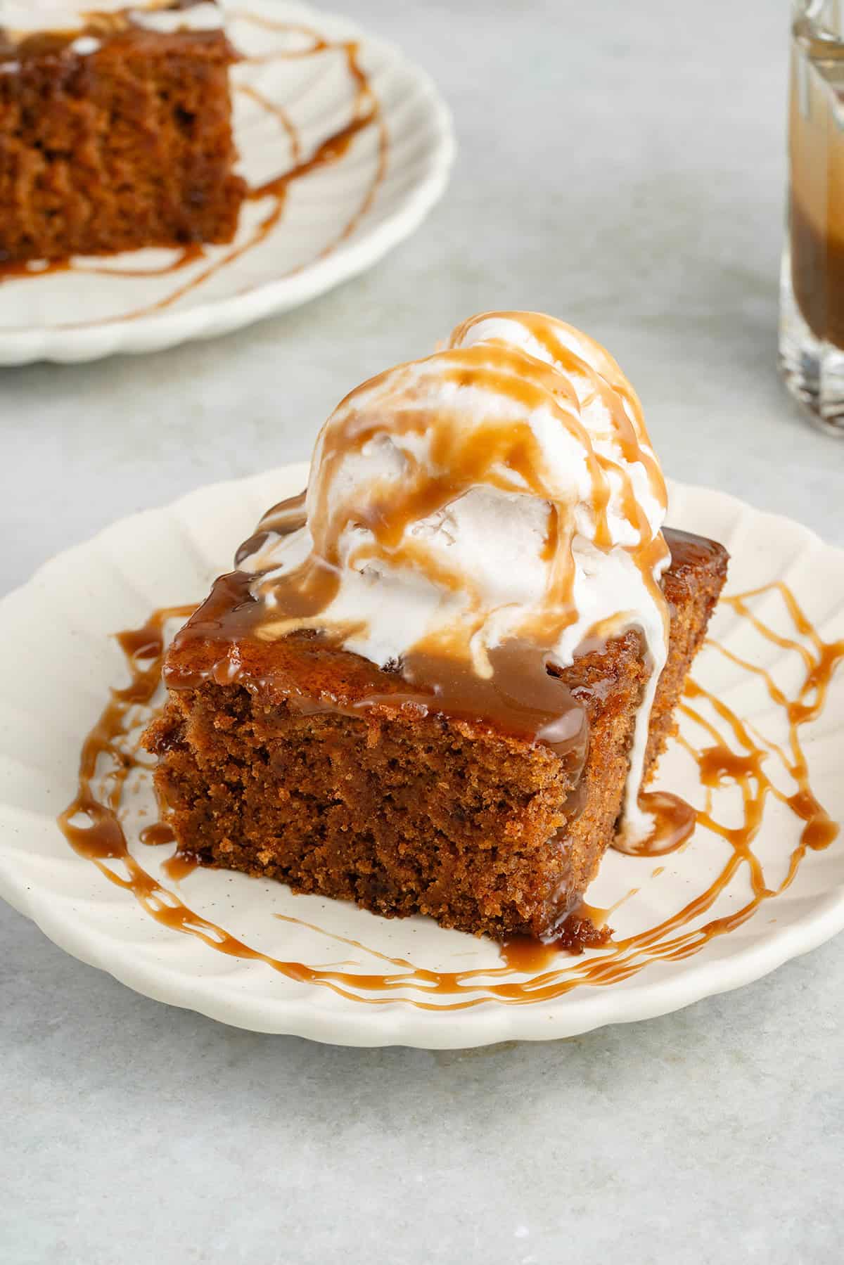 slice of chai sticky toffee pudding topped with ice cream and drizzled with caramel on a white plate
