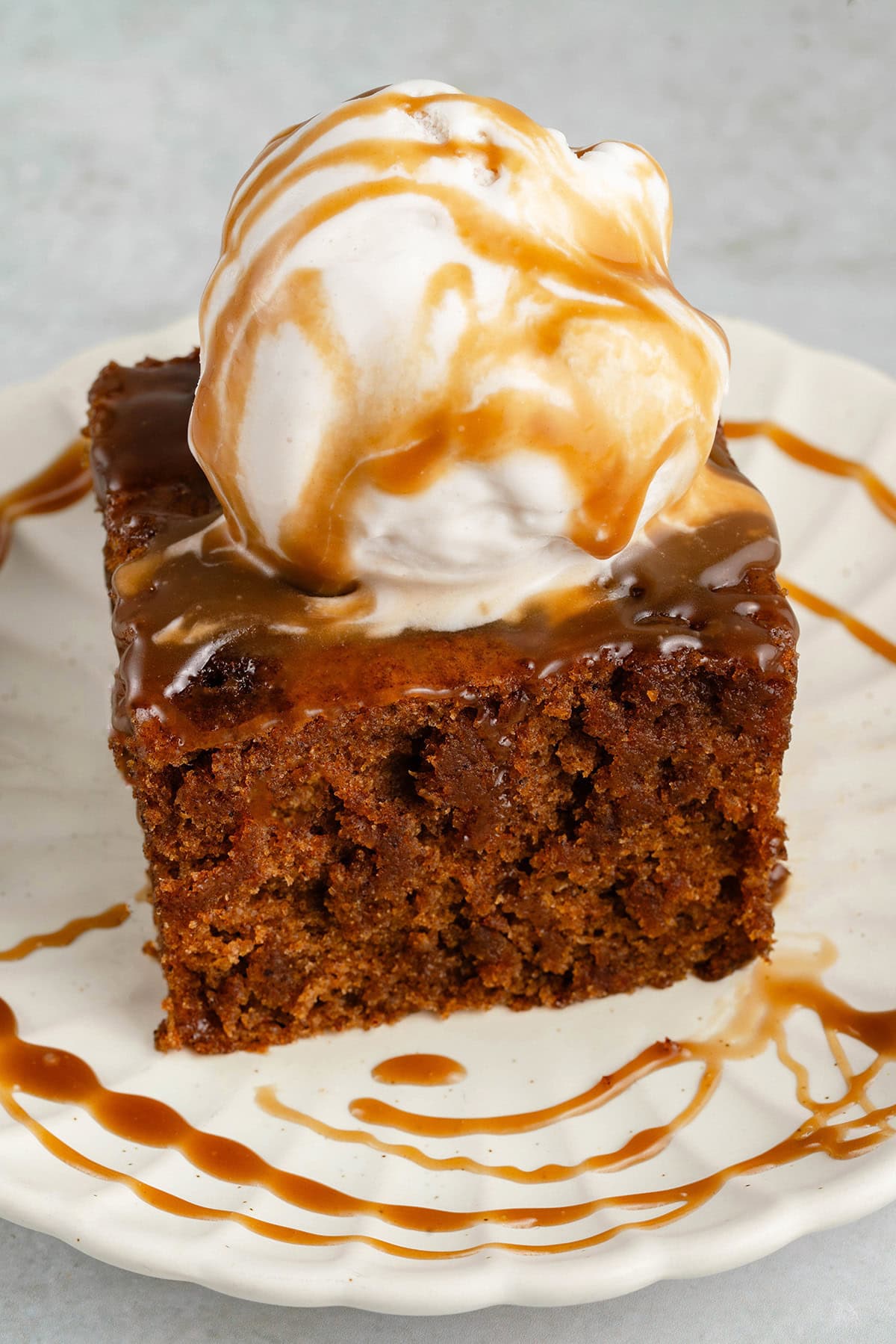slice of chai sticky toffee pudding topped with ice cream and drizzled with caramel on a white plate