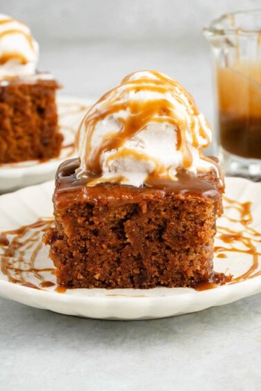 slice of chai sticky toffee pudding topped with ice cream and drizzled with caramel on a white plate