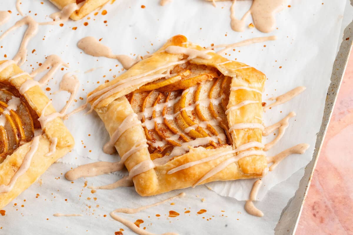 horizontal photo of Mini Spiced Pear Galettes with maple glaze on parchment paper