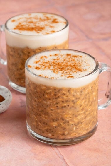 two glasses of pumpkin chai latte overnight oats on a pink background