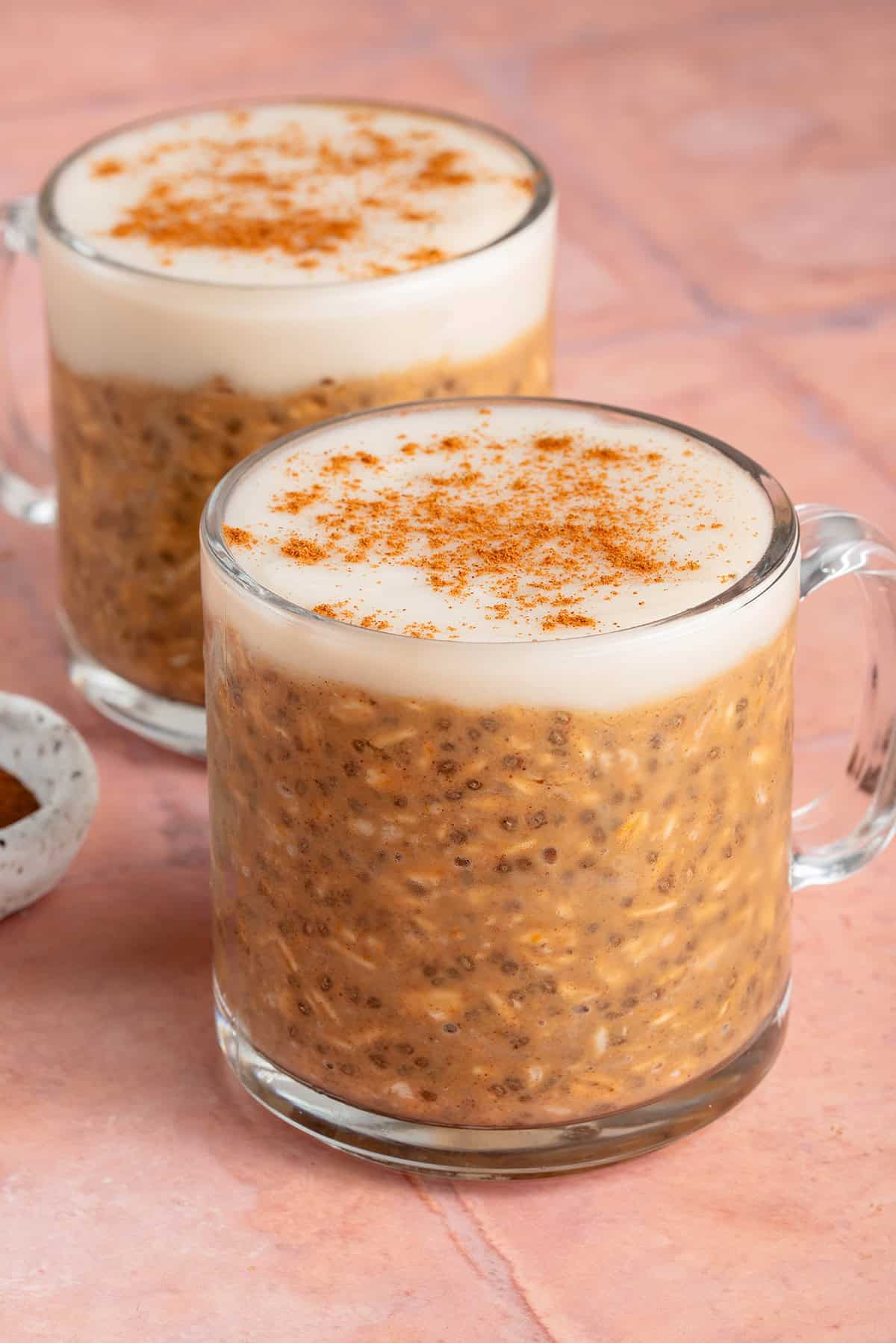 two glasses of pumpkin chai latte overnight oats on a pink background