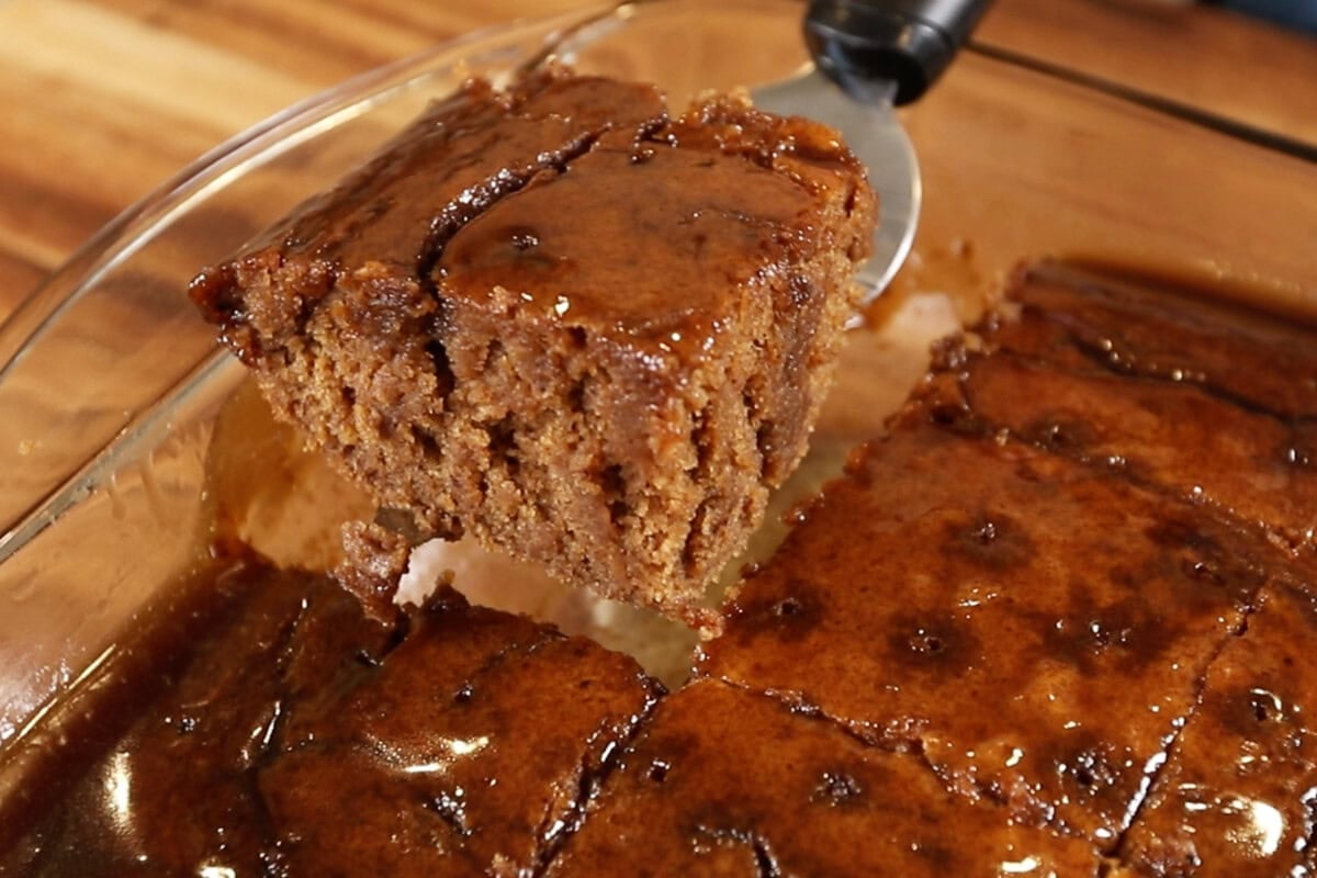 Lifting a slice of chai sticky toffee pudding out of tray with spatula
