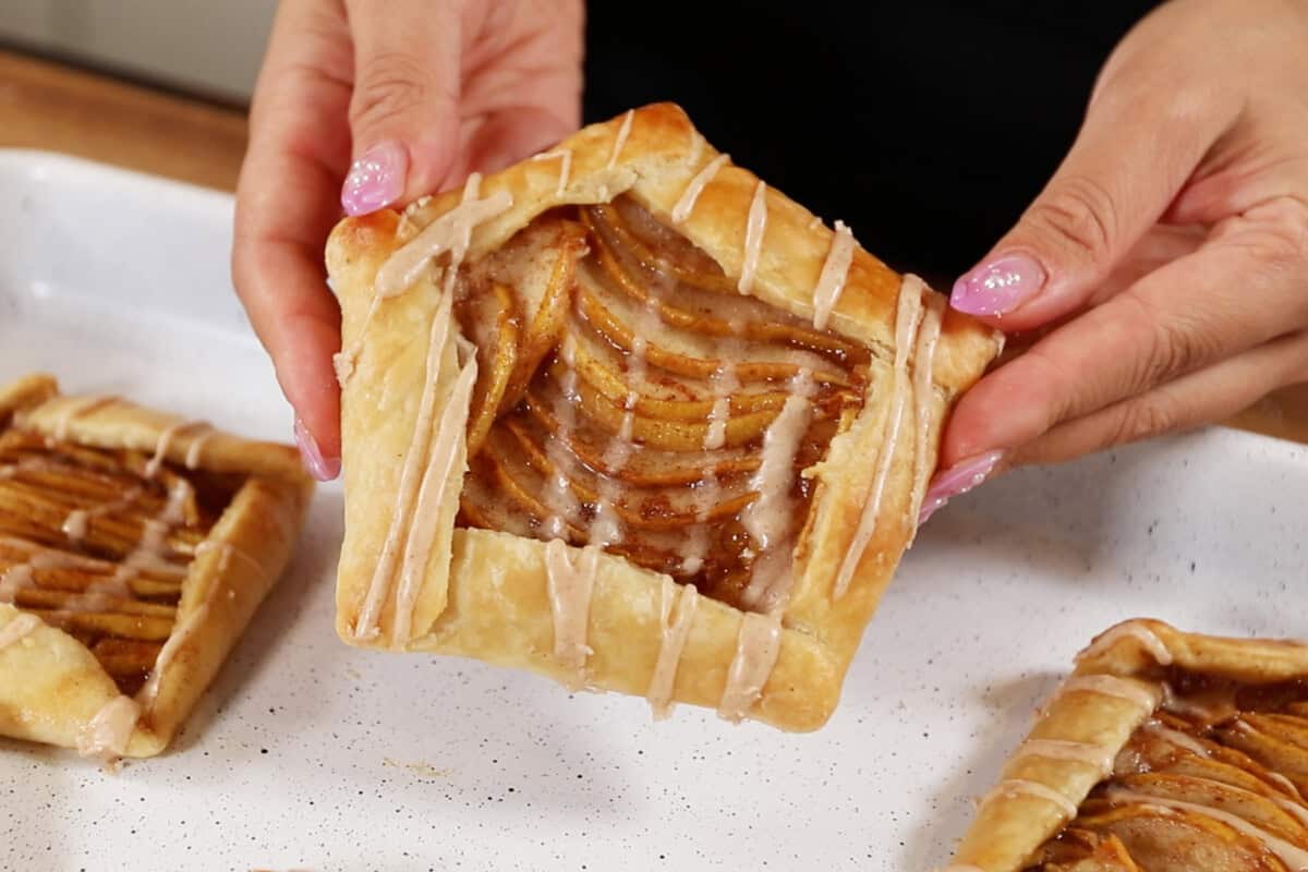 hands holding finished Mini Spiced Pear Galettes with maple glaze