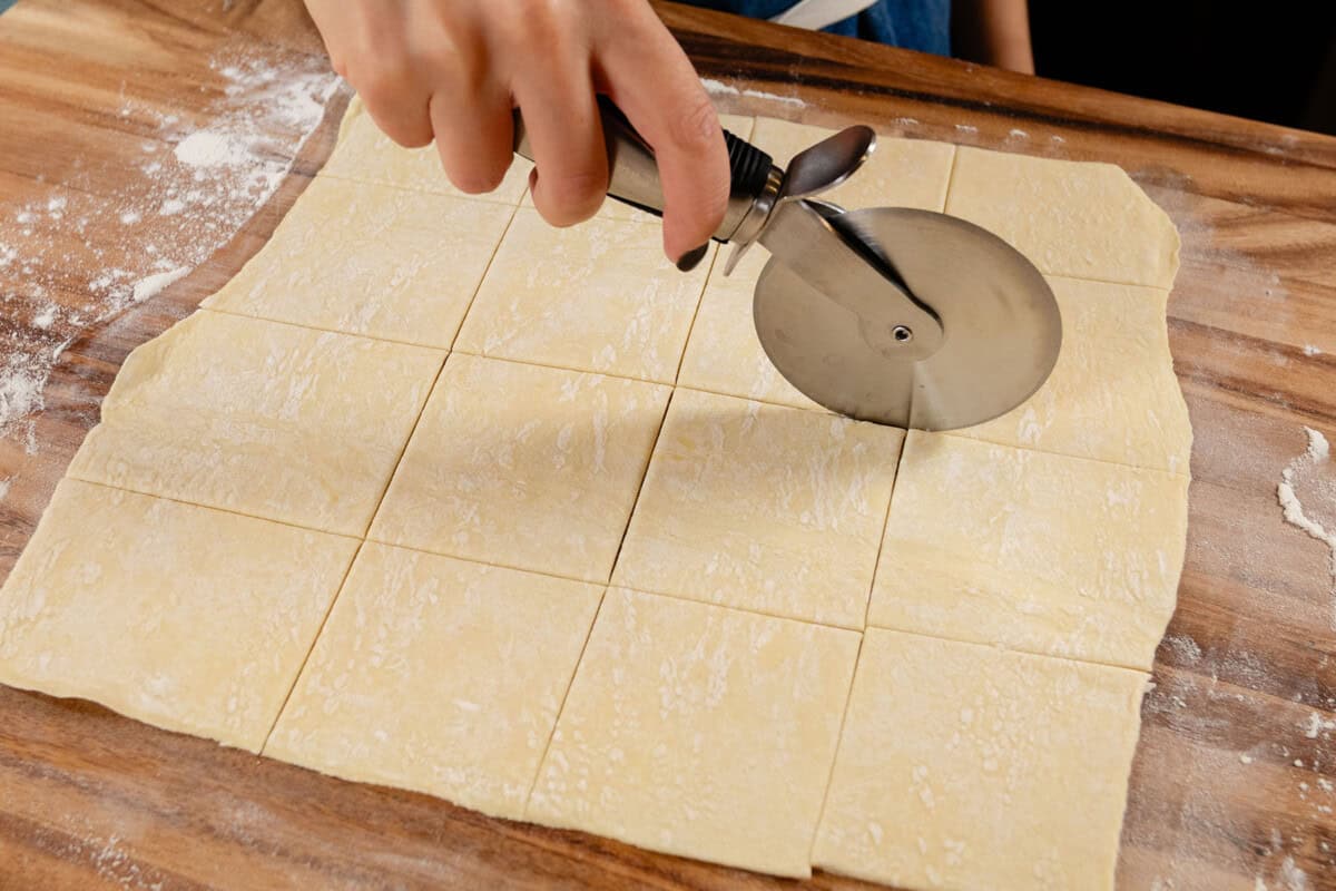 cutting puff pastry dough into squares for pot pie on a floured work surface